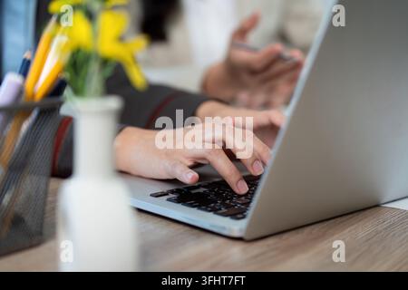 Two colleagues engage in a productive discussion at a modern workspace, focusing on project details while using a laptop. Stock Photo