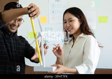 Two engineers measuring and discussing wind turbine models, highlighting sustainable engineering practices in a modern office setting. Stock Photo