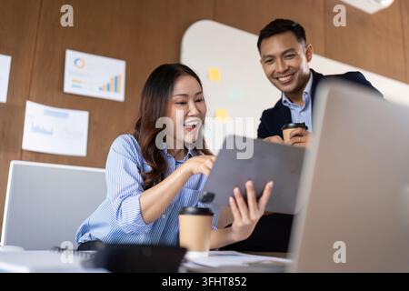 A business team collaborates enthusiastically over a digital tablet in a modern office, reflecting teamwork and innovation. Stock Photo