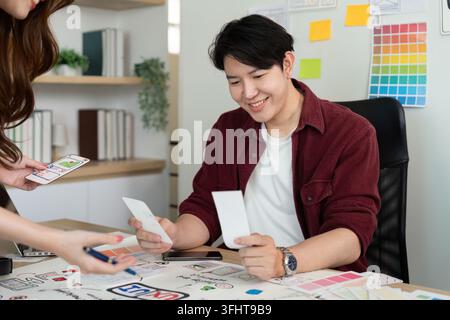 Two young designers engaged in a creative brainstorming session, reviewing sketches and digital mockups for user experience design. Stock Photo