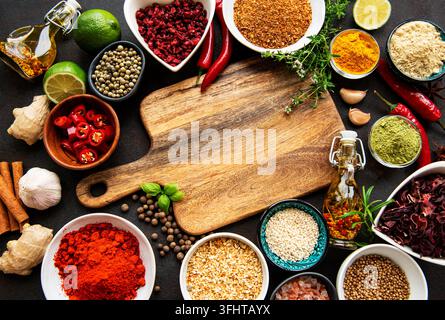 Various spices in a bowls and empty cutting board on black concrete background. Top view copy space. Stock Photo