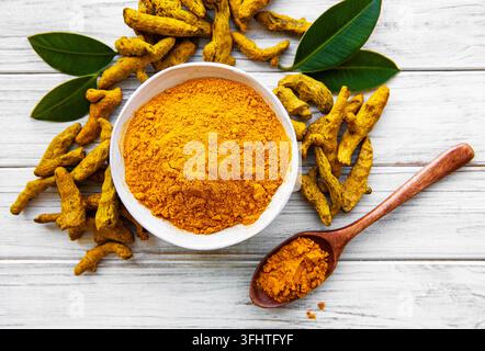 Bowl with turmeric powder and dry roots on a wooden background Stock Photo