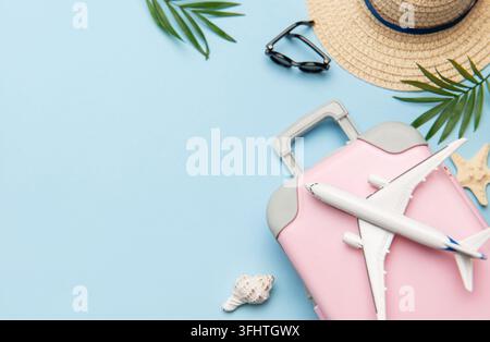 Pink suitcase with toy airplane, sunglasses, straw hat, seashells and palm leaves on blue background Stock Photo