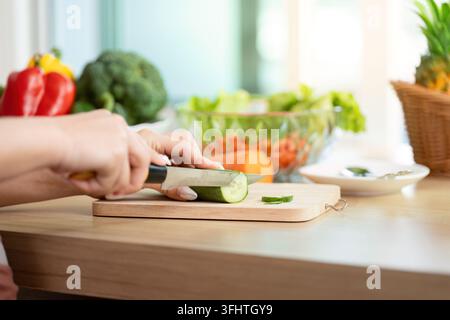 A woman skillfully slices cucumber, focusing on meal preparation and healthy eating in a bright kitchen environment. Stock Photo