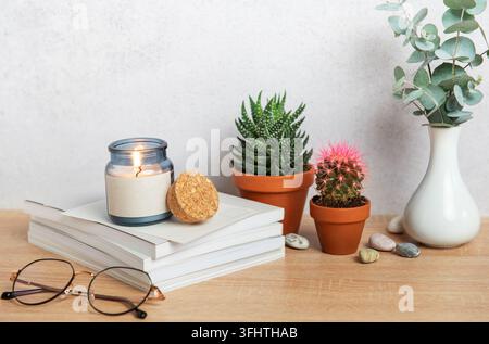 Burning candle, books, eyeglasses, plants and vase creating cozy atmosphere on wooden desk Stock Photo
