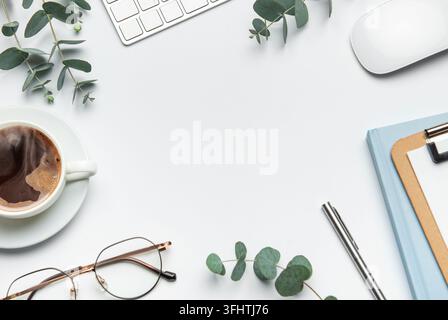 Eucalyptus branches, coffee cup, keyboard, mouse, glasses, pen, and notebook framing a white desk background, ideal for business or lifestyle blogs Stock Photo