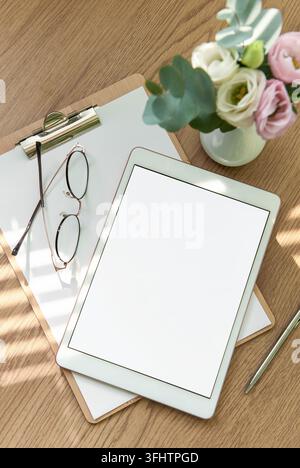 A bright workspace features a blank tablet, an open notebook, stationery tools, and fresh flowers arranged on a wooden table, inviting creativity and Stock Photo