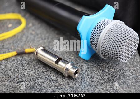 Professional microphone with blue clip and a metallic whistle on a stone surface Stock Photo