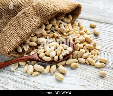 Peeled peanuts in a burlap bag on a white wooden background Stock Photo