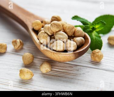 Peeled hazelnuts in a spoon on white wooden background Stock Photo