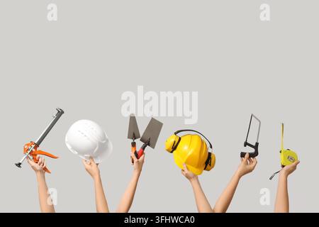 Hands with hardhats and construction tools on grey background Stock Photo