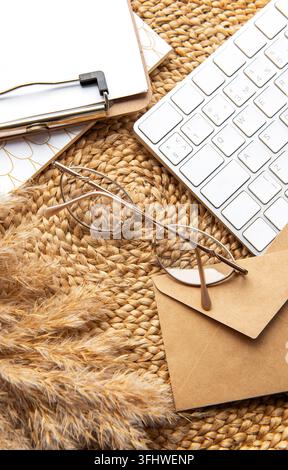 Flatlay of clipboard with blank paper sheet. Keyboard, pampas grass, stationery on beige straw background. Stock Photo