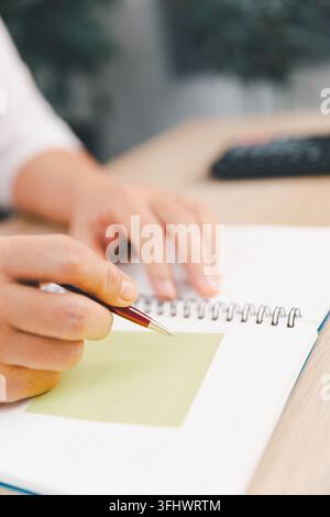 Close-up of a hand holding a pen over a blank sticky note in a spiral notebook, representing planning, reminder, note taking, organization, productivi Stock Photo