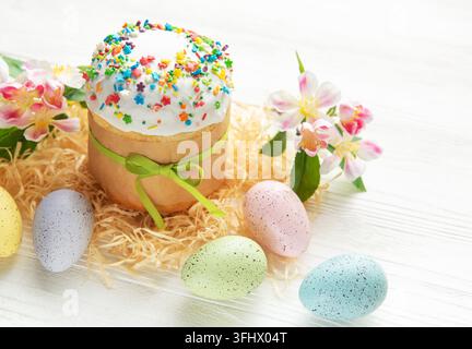 Traditional easter cake with colorful sugar sprinkles, pastel colored eggs and spring flowers on white wooden table Stock Photo