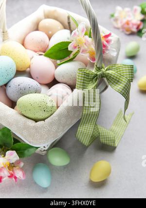 Pastel colored easter eggs overflowing from a white wicker basket decorated with spring flowers Stock Photo
