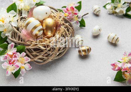 Easter eggs with gold and white decorations lying in a nest with spring flowers Stock Photo