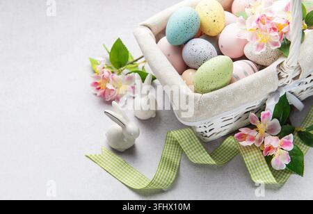 Pastel colored easter eggs overflowing from a white wicker basket decorated with spring flowers Stock Photo