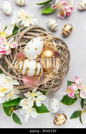Easter eggs with gold and white decorations lying in a nest with spring flowers Stock Photo