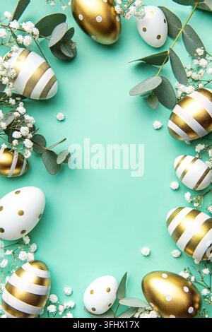 Easter eggs painted in gold and eucalyptus branches on a soft green background. Festive background Stock Photo
