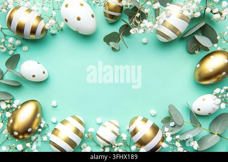 Easter eggs painted in gold and eucalyptus branches on a soft green background. Festive background Stock Photo