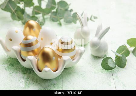 Easter decor. Golden Easter eggs on a ceramic holder and decorative rabbits. Stock Photo