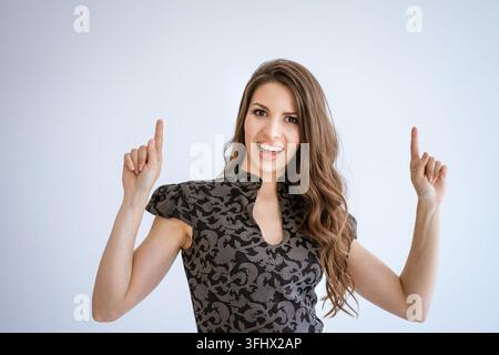 Woman in a dress poses on a white background, raises her fingers up Stock Photo