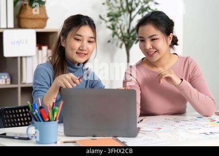 Two designers collaborating on UX and UI projects, sharing ideas and sketches while working on a laptop in a modern workspace. Stock Photo