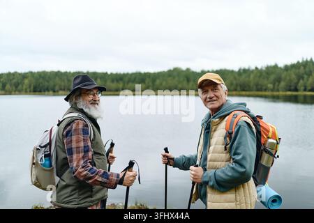 Two Active Senior Men Hiking with Trekking Poles by Lake Stock Photo