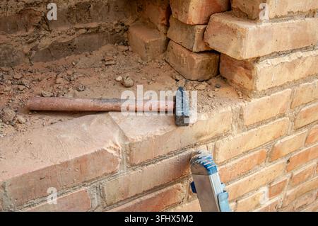 Hammer resting on a brick ledge amidst construction debris and stacked bricks Stock Photo