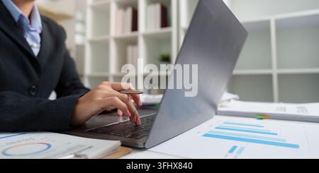 Digital Finance. Businesswoman typing on laptop while analyzing financial data. Stock Photo