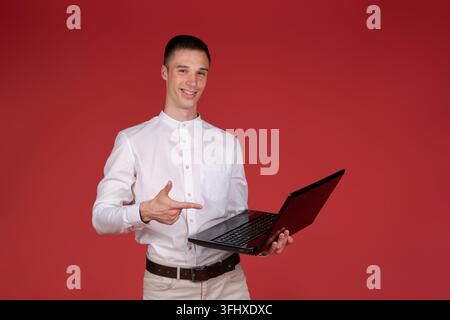 Young smiling successful businessman caucasian male in white shirt index finger on computer laptop isolated on red color background Stock Photo