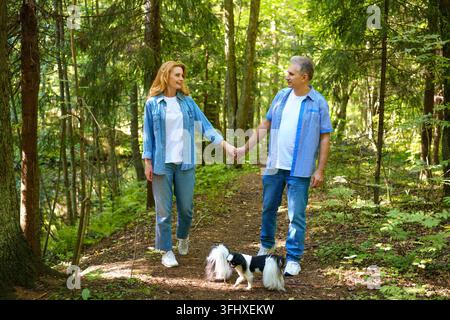 A mature couple is walking with a dog in a park. Man and woman in shirts and jeans. Stylish and modern grandparents. Stock Photo