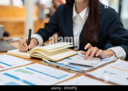 Businesswoman analyzing business graphs on their desks and calculating them using a calculator. Financial and accounting busines Stock Photo