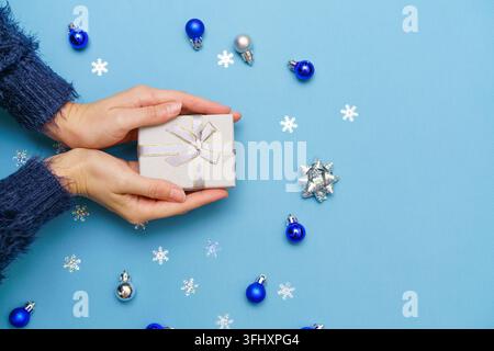Woman's hands holding gift box present, tied with ribbon bow on blue background Stock Photo
