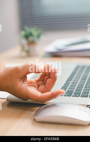 Close-up of hand making a calm meditation gesture beside laptop at office desk, representing mindfulness, stress relief, breathing break, focus, workp Stock Photo