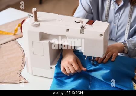 Fashion design and tailoring, dressmaker using a sewing machine to stitch blue fabric with pattern paper and measuring tape in a creative workshop Stock Photo