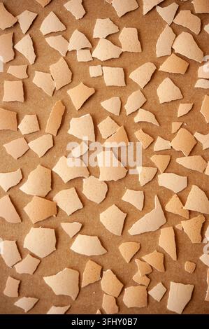 Broken eggshell shards scattered on a warm brown textured surface, photographed from above as an abstract archaeological still life Stock Photo