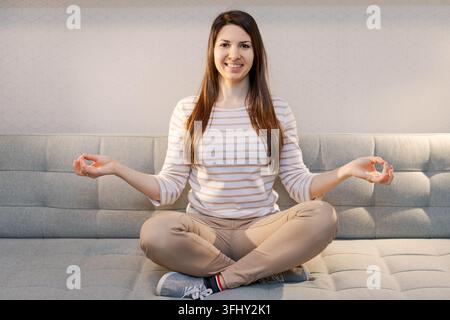 A woman is sitting on a couch and practicing yoga Stock Photo