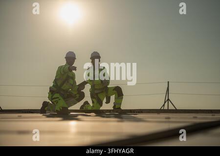 Male and female engineers inspecting solar panel installation points on a rooftop under sunlight, representing clean energy and sustainable developmen Stock Photo