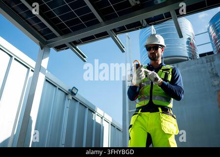 Engineer inspecting electrical wiring and connections beneath rooftop solar panels, emphasizing safety standards and photovoltaic system efficiency Stock Photo