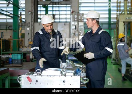 Industrial engineers and technicians discussing machine operation while inspecting equipment in a manufacturing factory Stock Photo