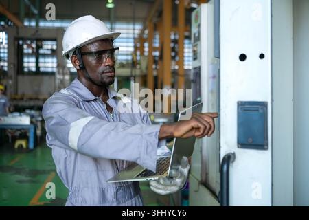 Industrial technician using a laptop computer to monitor machinery systems and production processes in a manufacturing factory Stock Photo