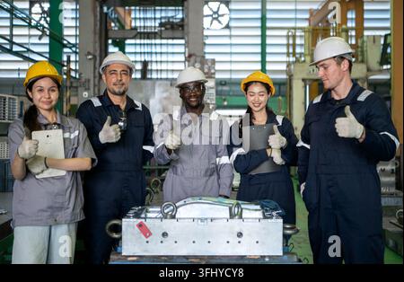 Diverse group of industrial engineers and factory workers standing together in a manufacturing plant wearing safety helmets and work uniforms Stock Photo