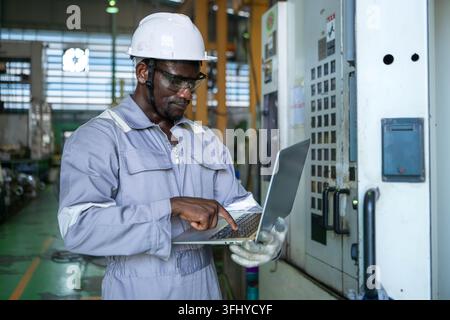 Industrial technician using a laptop computer to monitor machinery systems and production processes in a manufacturing factory Stock Photo