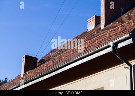 The pitched roof surface features brown ceramic tiles equipped with metal snow retention guards under a bright sky, highlighting classic building mate Stock Photo