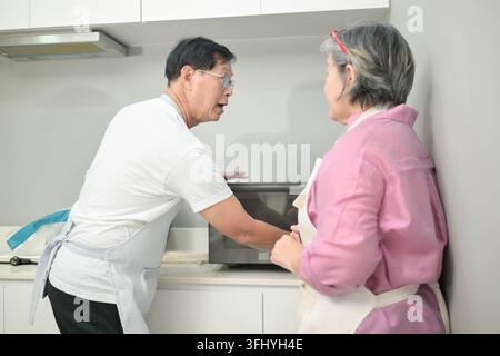 Asian senior couple using a microwave oven together in the kitchen, representing everyday cooking and shared domestic life Stock Photo