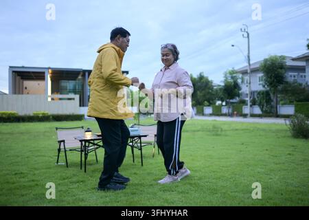 Happy Asian senior couple dancing together in a garden near their home, enjoying a joyful and active retirement lifestyle outdoors Stock Photo