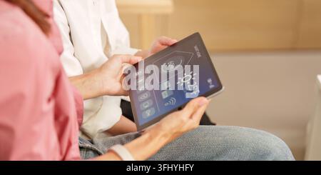 Close-up of a tablet displaying a smart home interface, held by a person in a casual home setting. Stock Photo