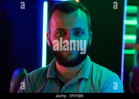 Confident bearded man poses for a close-up portrait illuminated by colorful neon lights in a gaming and technology environment, conveying focus, moder Stock Photo