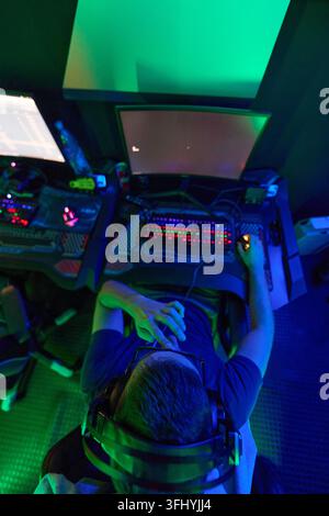 Overhead view of a gamer wearing headphones at a PC desk, using a glowing RGB keyboard and mouse in a neon-lit gaming room, conveying focus, immersion Stock Photo